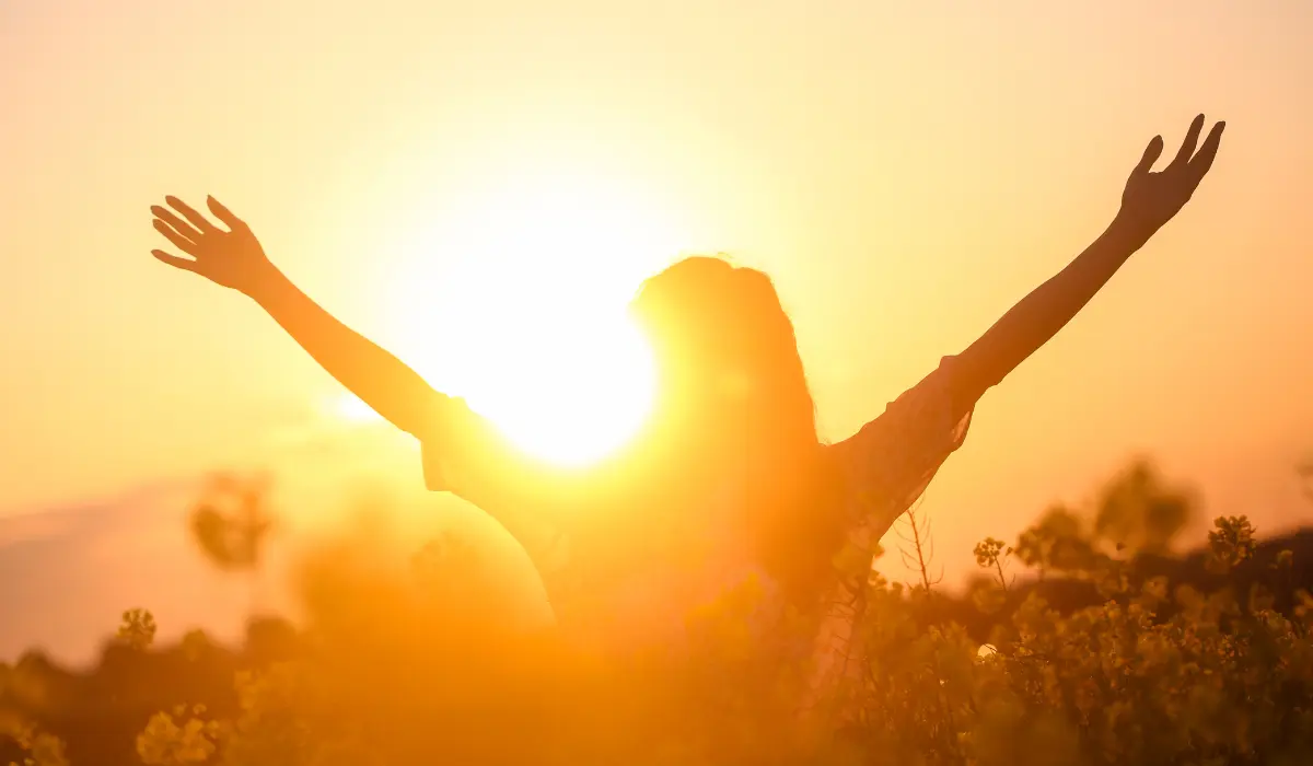 jeune femme bras en l'air devant le soleil